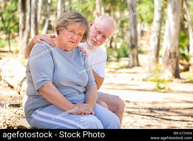 Very upset senior woman sits with concerned husband outdoors