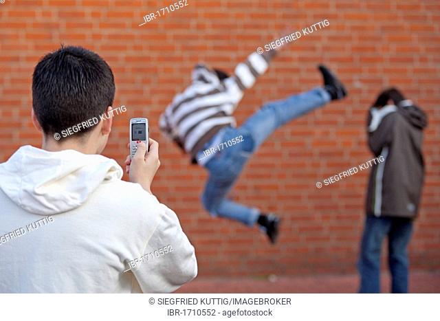Boy attacking another boy with a karate kick while a third films with his cell phone, posed scene