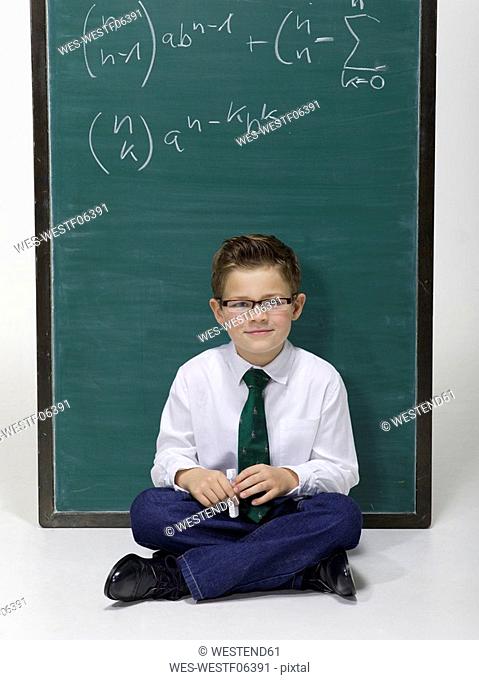 Boy 10-11 sitting in front of blackboard, portrait