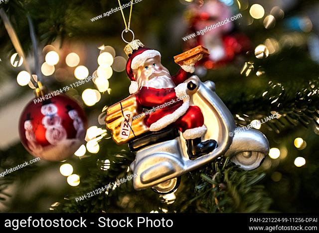 24 December 2022, Lower Saxony, Göttingen: A Christmas tree is decorated with a Santa Claus figure on a motorcycle, a string of lights and Christmas balls