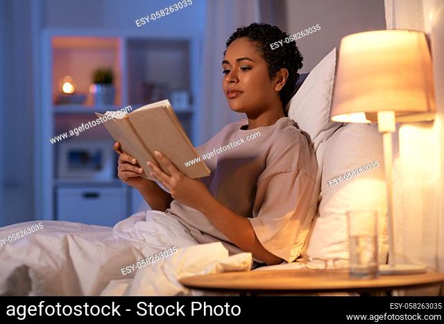 young woman reading book in bed at home