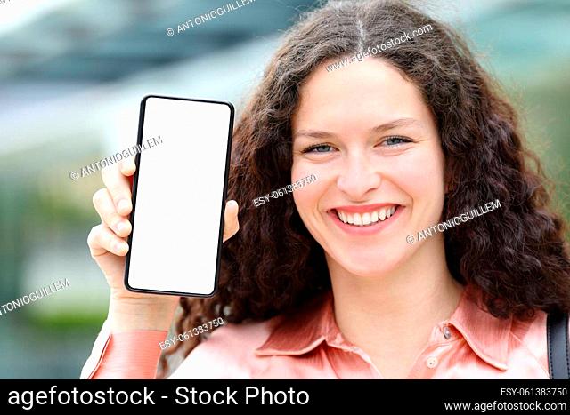 Front view of an elegant happy woman with blouse showing blank phone screen in the street