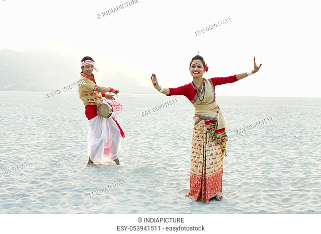 Bihu woman dancing as Bihu man plays on a dhol
