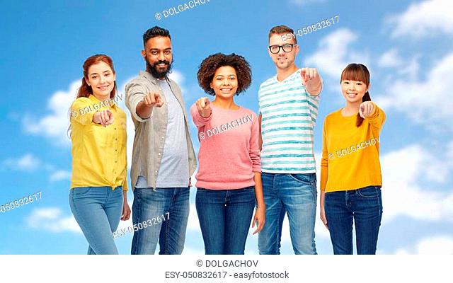 diversity, race, ethnicity and people concept - international group of happy smiling men and women pointing finger on you over blue sky and clouds background