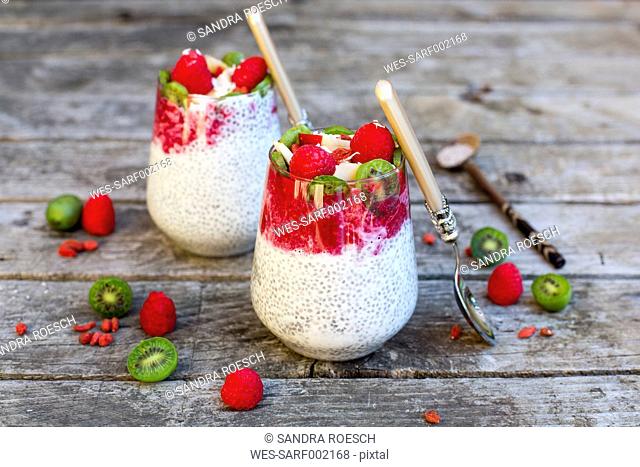 Two glasses of chia pudding with cocos, raspberry sauce and several fruits