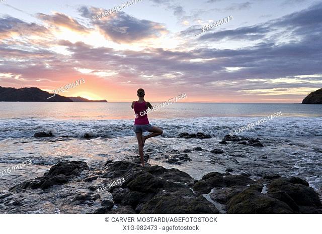 Young woman doing yoga at sunset in front of ocean surf at Playas del Coco, Costa Rica