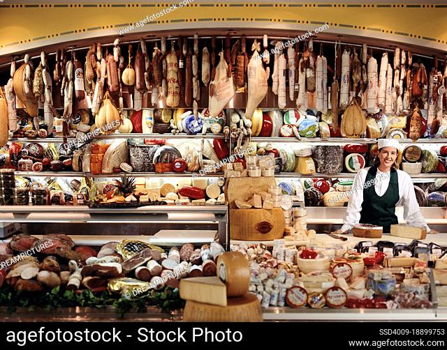 Associate in Chefs hat at deli counter with large selection of imported meats and cheeses