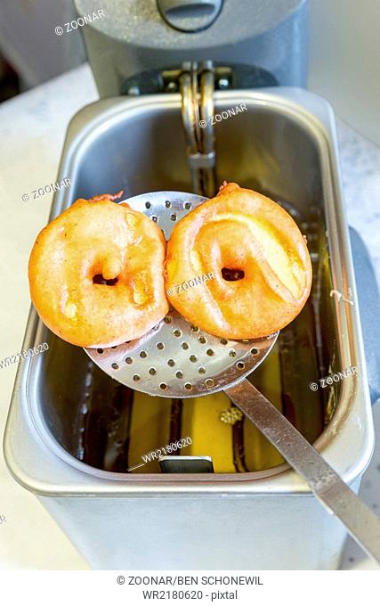 Apple turnovers on spoon above frying oil