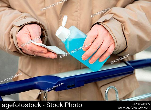 Mans Hand hold a plastic bottle with disinfectants, for using the handle of a shopping cart get disinfected