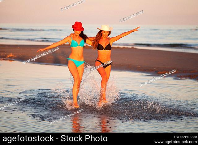 Two beautiful girls in bikinis walking on the beach at sunset