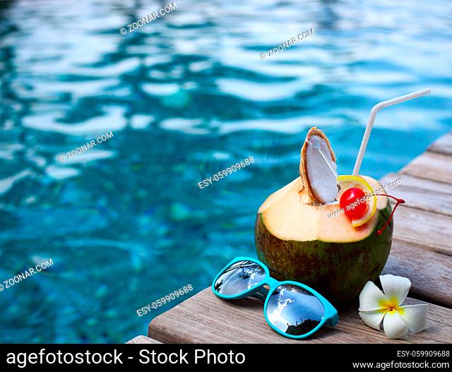 Coconut cocktail with drinking straw by the swimming pool with the sunglasses