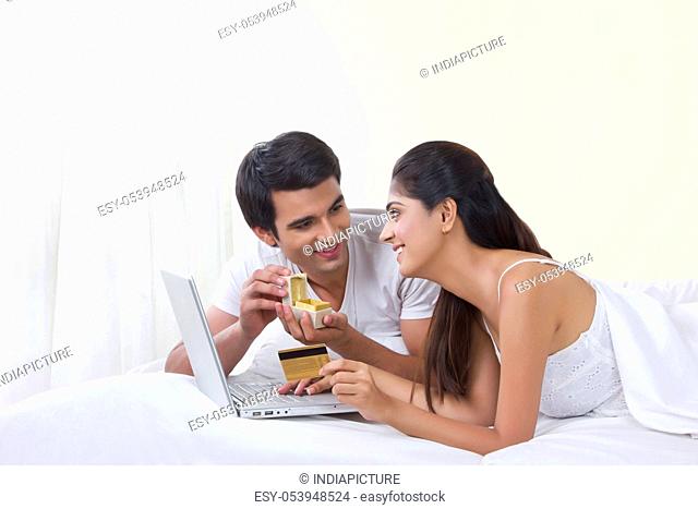 Happy couple buying ring online with credit card in bed