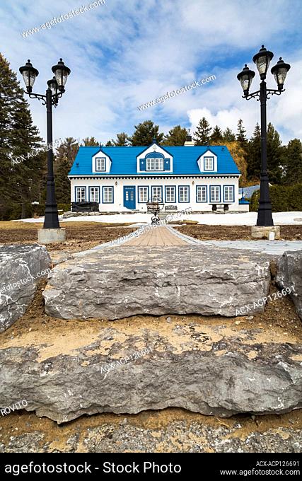 Back view of old 1920s white roughcast with blue trim cottage style house with blue steel tile roof in early spring, Quebec, Canada