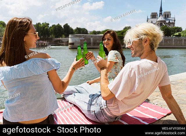 Man smiling while raising toasts with female friends during sunny day