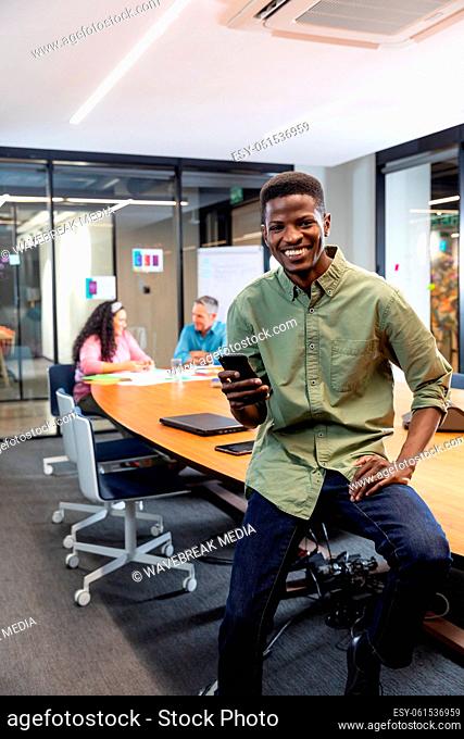 Portrait of smiling african american businessman with smart phone while colleagues in background