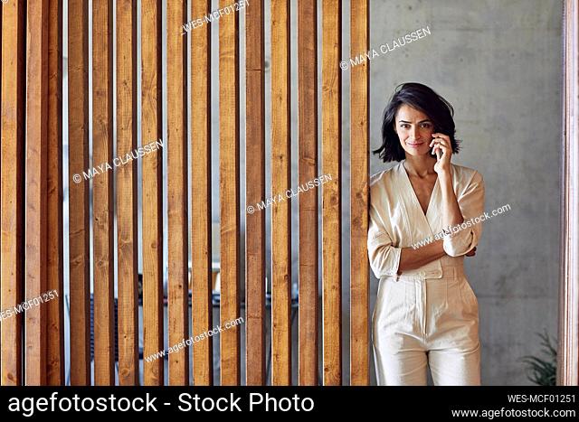 Businesswoman talking over smart phone while standing by wooden door in office