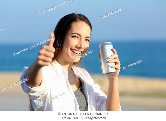 Portrait of a happy woman holding a refreshment can looking at you on the beach
