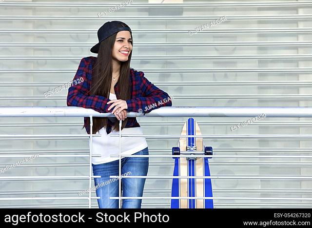 Shot of smiling female in cap standing near skate while posing for camera looking away