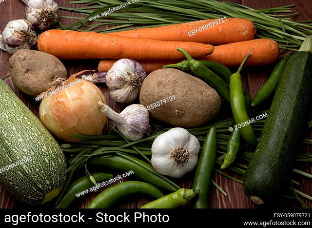 A close up of a bunch of assorted vegetables such as garlic, carrots, chives, onions, potatoes, and peppers