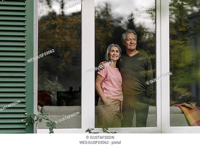 Senior couple behind windowpane of their home looking out