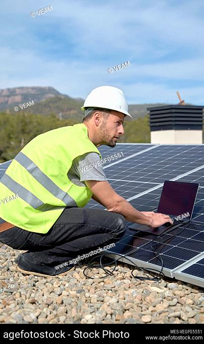 Engineer with laptop by solar panels on sunny day