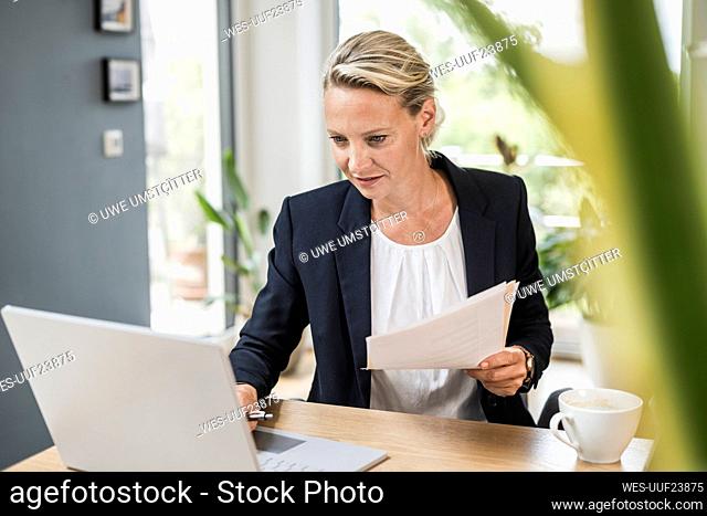 Businesswoman holding document while using laptop at office