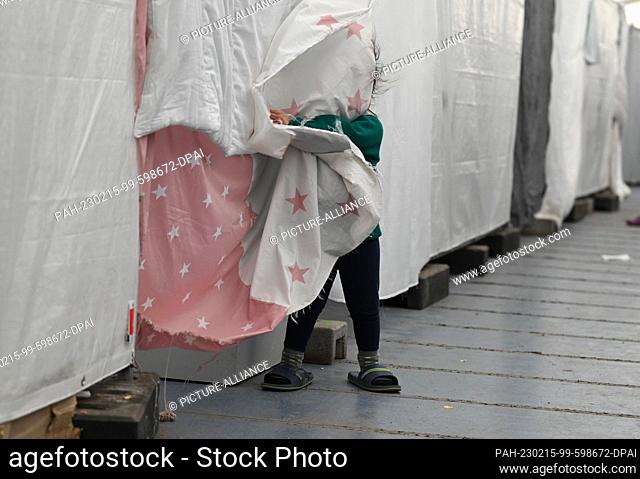 PRODUCTION - 10 February 2023, Hesse, Bensheim: A refugee child from Turkey stands in a tent of the refugee shelter in front of a residential lot