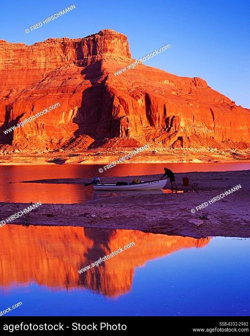 Morning reflection of Tim Pfeiffer loading Bristol Skiff on shore of Lake Powell near mouth of Dungeon Canyon, Glen Canyon National Recreation Area, Utah