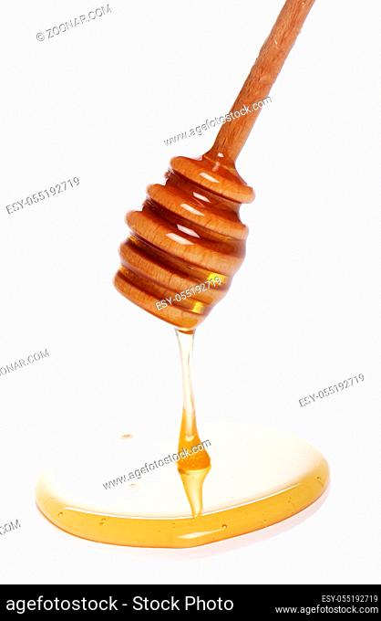 Honey dripping from a wooden spoon over white background