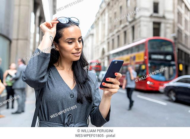 Business woman near a busy street checking her smartphone, London, UK