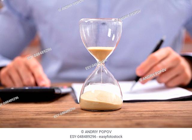 Close-up Of A Hourglass In Front Of Businessman Working In Office