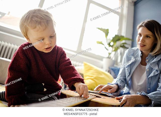 Baby boy exploring a guitar with his mother