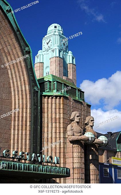 Clock tower and two pairs of statues made of granite holding the spherical lamps at the entrance to the Central railway station, Helsinki, Finland
