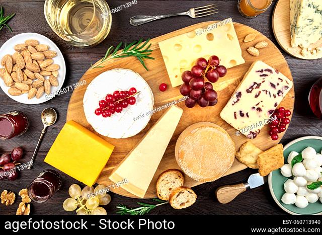 An assortment of various types of cheese with wine, and grapes, shot from above on a dark rustic background