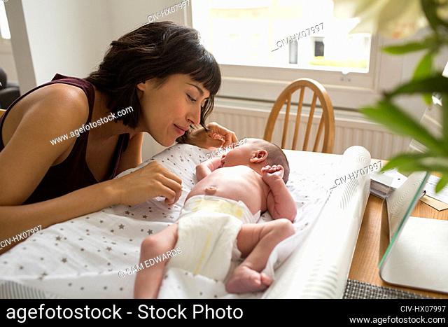Loving mother watching newborn baby son laying on changing table