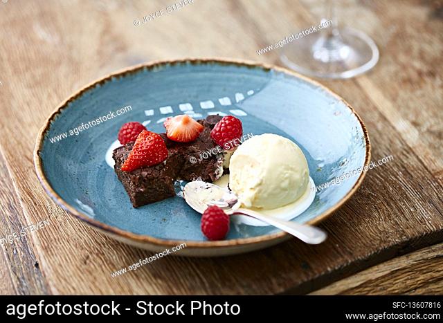 Chocolate brownie topped with strawberries and raspberries with a vanilla ice cream