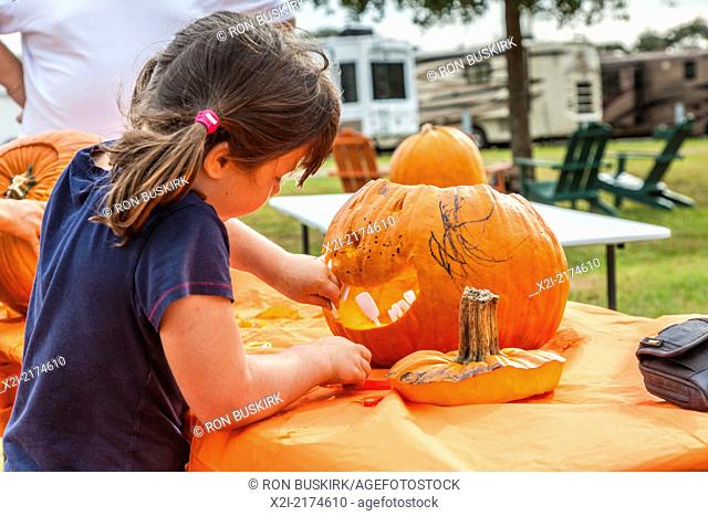 Young girl inserts teeth while decorating a pumpkin for Halloween in an RV resort park in Florida