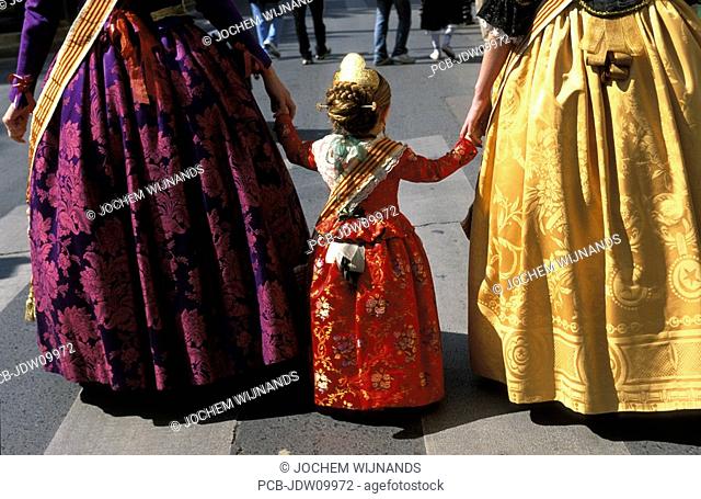Valencia, a girl beeing accompanied two women in traditional costumes in the procession to the Plaza de la Virgen with a floral offering to Our Lady of the...