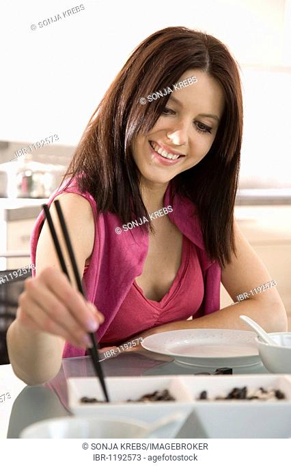 Young woman sitting at laid table, eating with chopsticks