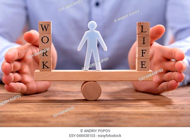 Human Figure Standing Between Work And Life Wooden Blocks On Seesaw Being Protected By Businessperson