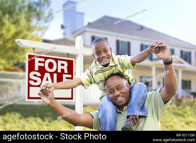 Happy african american father and son in front of home and for sale real estate sign