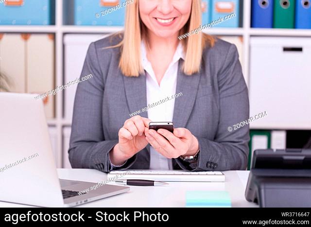 Woman at the office typing and messaging with her mobile phone