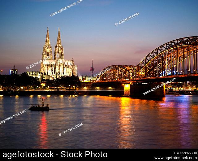 Koelner Dom Sankt Petrus (meaning St Peter Cathedral) gothic church and Hohenzollernbruecke (meaning Hohenzollern Bridge) crossing the river Rhein at night in...