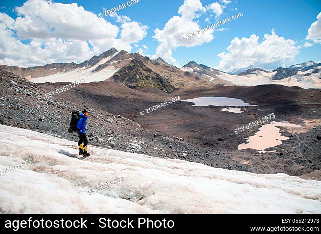 Traveler in a cap and sunglasses with a backpack on his shoulders in the snowy mountains on the glacier against the sky and clouds