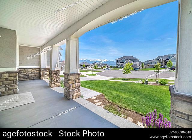Porch with pillars and a combination of concrete and stone brick exterior walls. It has a view of the yard, neighborhood, mountain, and blue sky