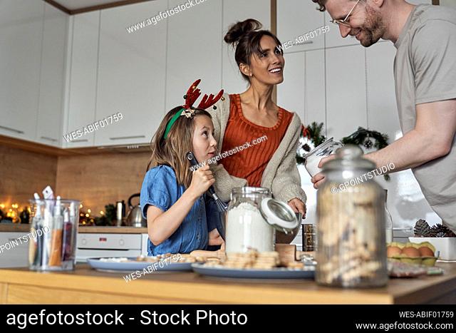 Smiling parents with daughter preparing cookie dough in kitchen