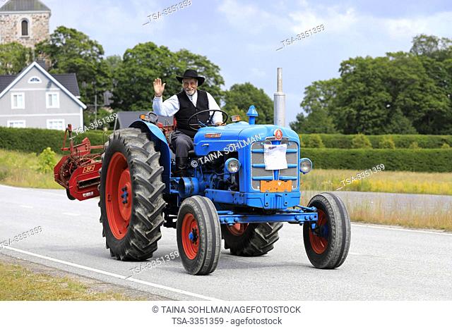Kimito, Finland. July 6, 2019. Man in traditional costume greets as he drives Fordson Super Major on Kimito Traktorkavalkad, vintage tractor parade