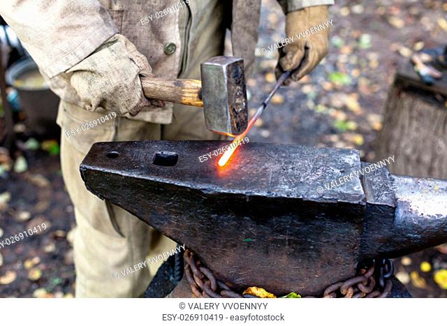 Blacksmith hammering hot steel rod on anvil in outdoor rural smithy