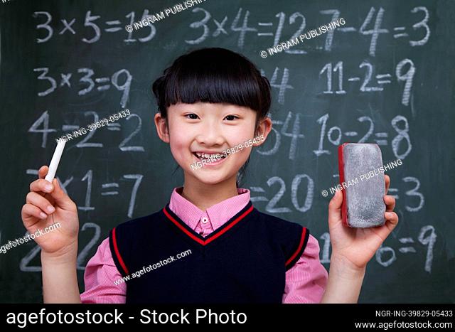 Portrait of schoolgirl in front of blackboard holding chalk and eraser