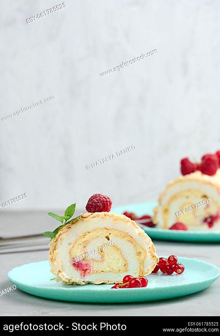 Baked meringue roll with red berries on a round plate, white background